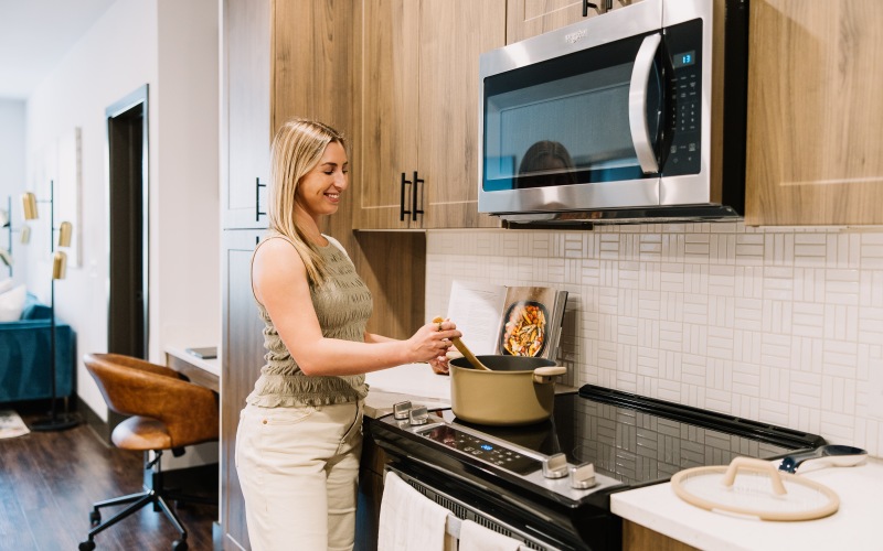A woman stirring pasta sauce on a stovetop in the kitchen at The Harden at Public Market apartments in fort worth