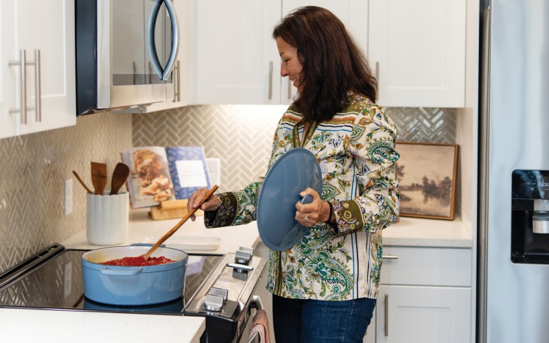 A woman stirring pasta sauce on a stovetop in the kitchen at The Harden at Public Market apartments in fort worth